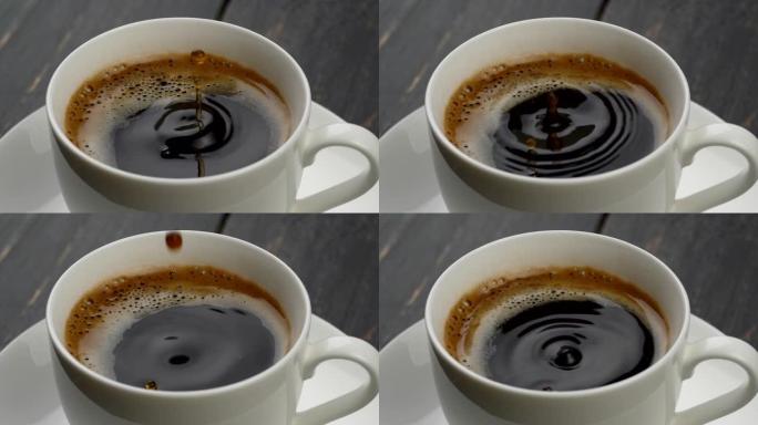 一杯咖啡特写。圆形的咖啡水滴落入黑色，橙色的泡沫中，咖啡在白色的杯子里，放在白色的碟子上。慢动作镜头