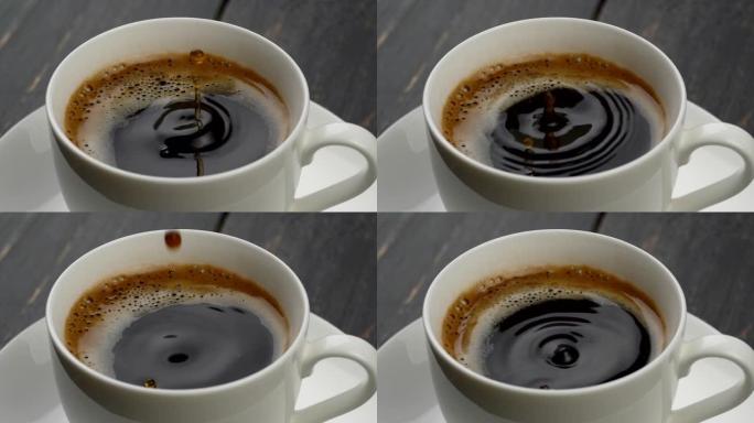 一杯咖啡特写。圆形的咖啡水滴落入黑色，橙色的泡沫中，咖啡在白色的杯子里，放在白色的碟子上。慢动作镜头