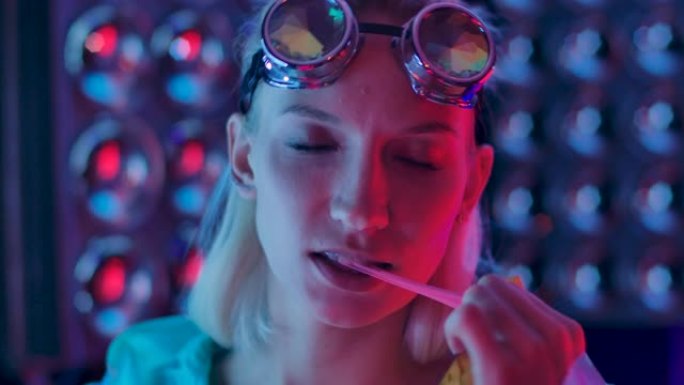 20多岁可爱的女孩嚼泡泡糖。年轻性感俏皮的金发女士站在俱乐部的肖像穿着粉红色的蓝色光线和咀嚼糖果。女