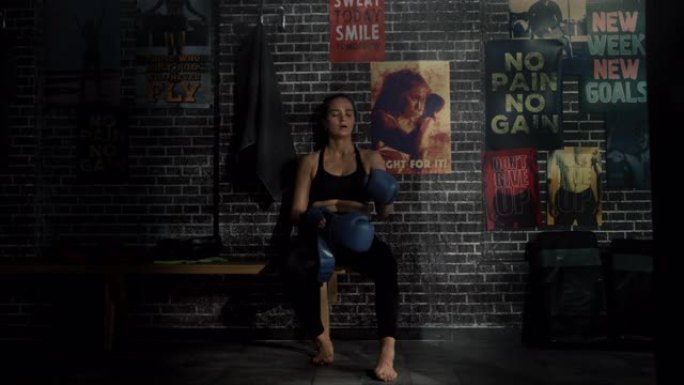美丽健康的黑发跆拳道运动员坐在阁楼健身房的长凳上，拿着励志海报。她屏住呼吸，脱下战斗手套。经过紧张的