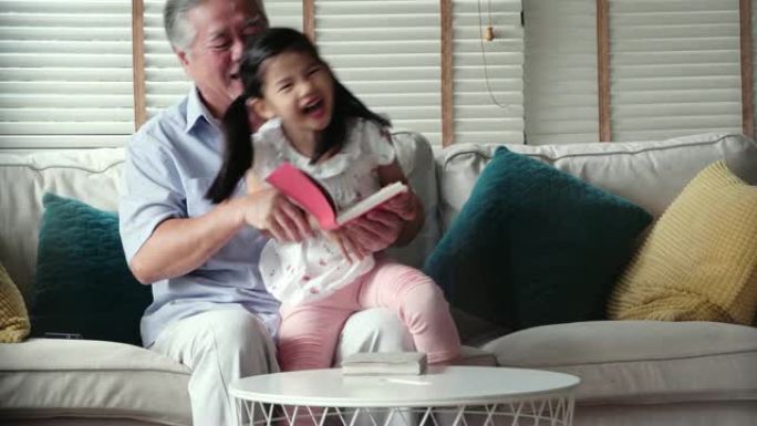 快乐的小女孩和爷爷在家读故事书。香港的家庭