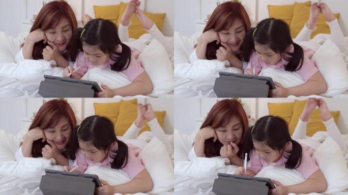 亚洲祖母用平板电脑在家给孙女读童话故事。高年级中国人，奶奶开心放松年轻女孩睡前躺在床上晚上在家卧室的