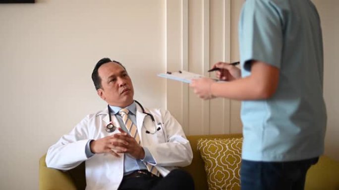 一名亚洲男医生坐在沙发上与一名男护士就患者病例进行交谈