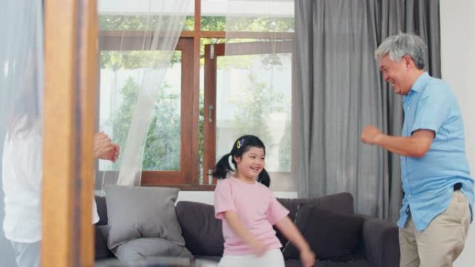 亚洲祖父母和孙女在家里一起听音乐和跳舞。高级中国人，爷爷和奶奶开心地与客厅概念中的年轻女孩一起度过家