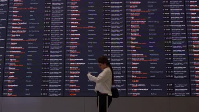 拉丁美洲妇女在机场看着航班时刻表屏幕，同时看着登机牌和护照