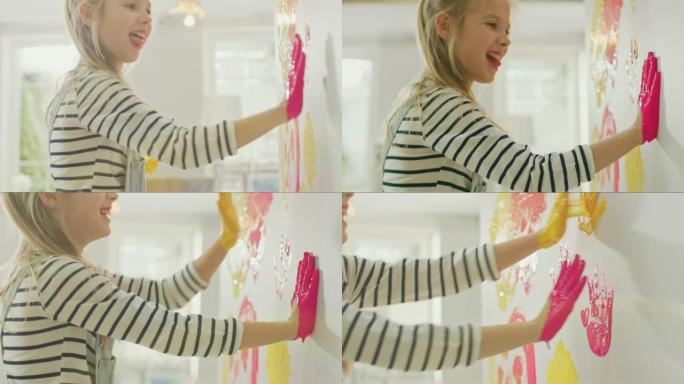双手蘸黄色和粉红色油漆的快乐小女孩在墙上贴了五颜六色的手印。她玩得很开心，笑得很开心。家正在装修。