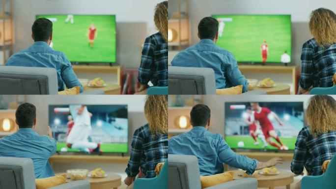 在家里，年轻夫妇在电视上观看足球比赛，体育迷在情感上为他的球队打手势，忧虑和欢呼。倒车摄像头拍摄。
