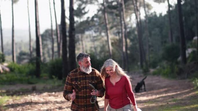 高年级高加索夫妇带着狗在松树森林徒步旅行