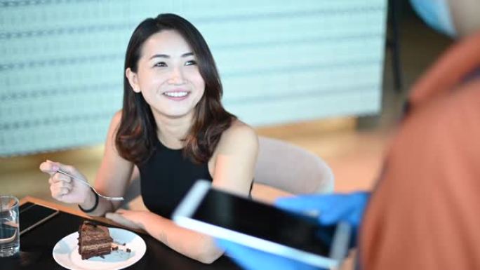 一位亚洲华人小型企业咖啡馆老板女士与顾客交谈，以新的正常社会距离标准操作程序在咖啡馆订购