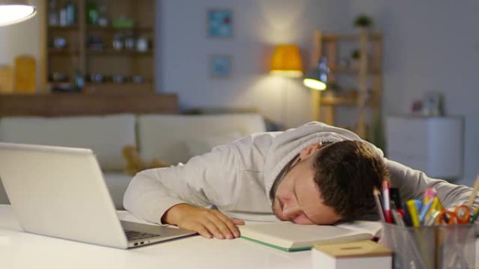 精疲力竭的男人睡在客厅的桌子上，笔记本电脑