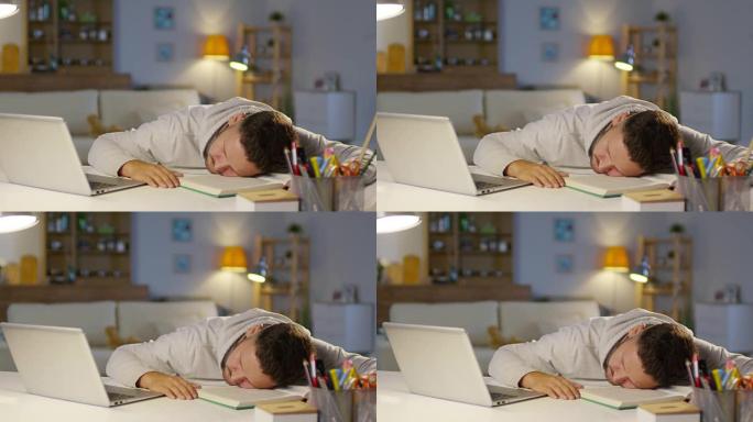 精疲力竭的男人睡在客厅的桌子上，笔记本电脑