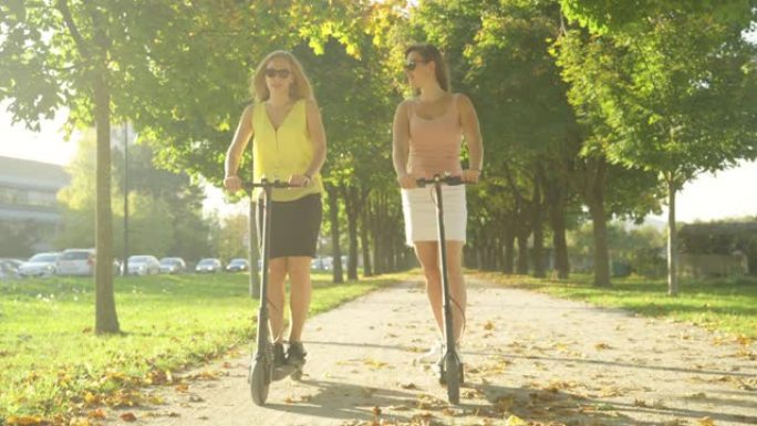 SUN FLARE: 两个女人在公园周围骑电动踏板车时微笑着说话