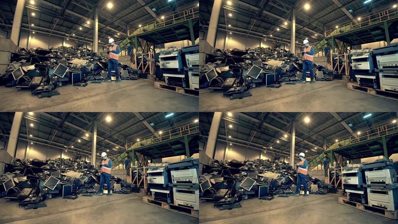 回收工业，二手电子回收工厂。垃圾填埋场工人在一堆杂物附近用智能手机