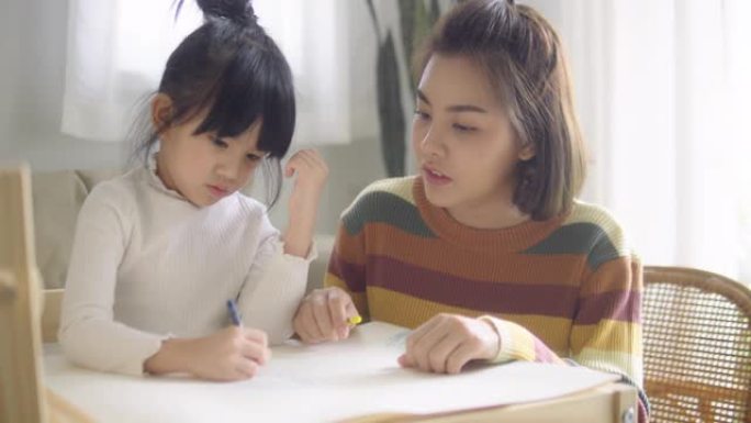 在母亲的帮助下，可爱可爱的亚洲女孩在家做作业。