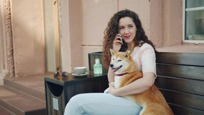 年轻的女士在咖啡馆里用手机说话，在户外拥抱柴犬