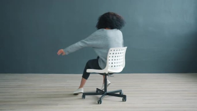 灰色背景上在办公椅上旋转的顽皮非洲裔美国女孩的肖像