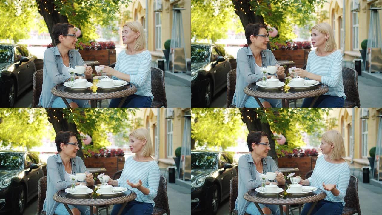 迷人的女士朋友在户外咖啡馆聊天，手里拿着咖啡杯微笑