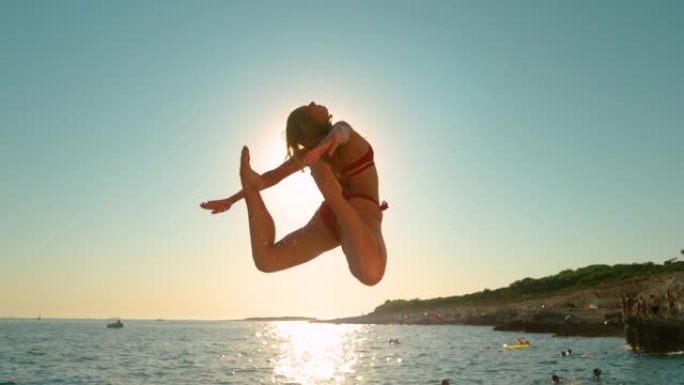 镜头耀斑: 金色的早晨阳光照耀着年轻敏捷的女子悬崖跳水。