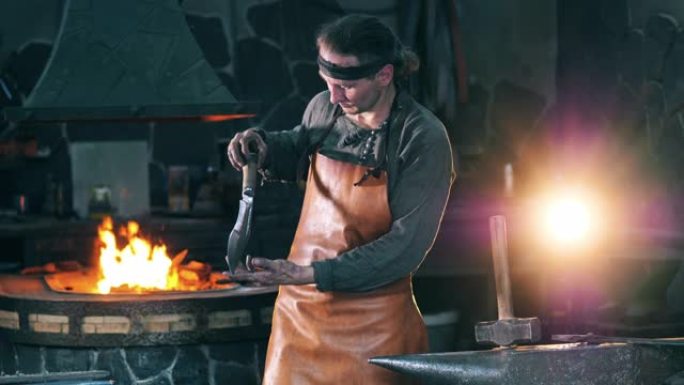 专业铁匠看着一把金属刀，站在铁匠铺上。