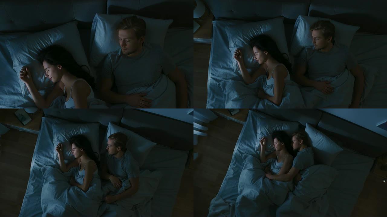 晚上的俯视图床: 迷人的年轻夫妇睡在一起，互相拥抱。蓝色夜间颜色，寒冷微弱的灯柱光线透过窗户照射。