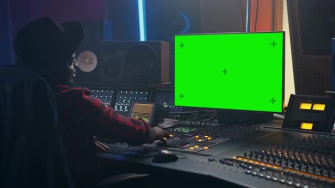 在音乐录音室工作的时尚男性音频工程师制作人的肖像，使用绿屏计算机，控制台创作新歌。富有创造力的黑人艺
