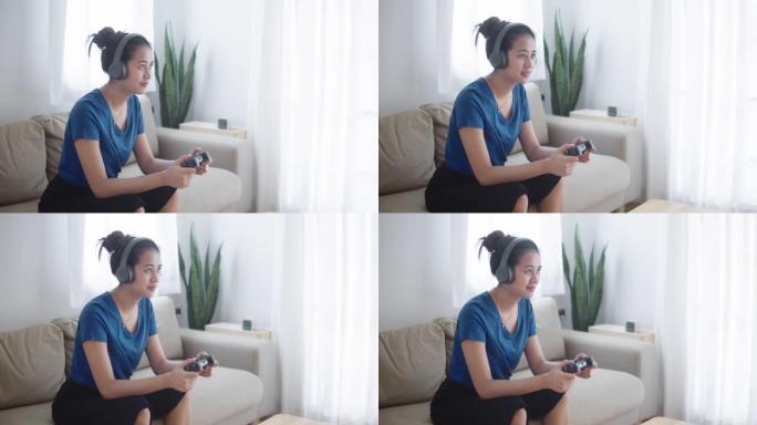 年轻的亚洲女孩玩电子游戏，在家沙发上拿着游戏控制器。