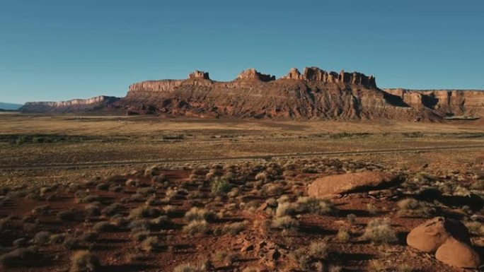 无人机在一条小路上低空飞行在干燥的砂岩沙漠和卡车上，令人惊叹的美国阳光明媚的平坦山脉天际线。