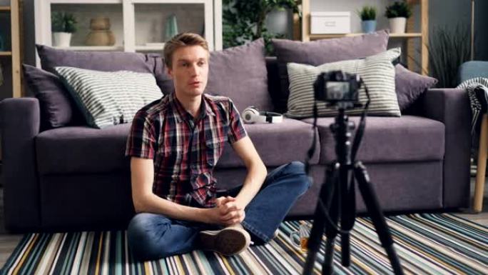 年轻人正坐在家里的地板上为他的在线博客录制视频