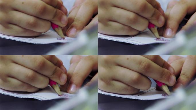 一个用粉红色铅笔画纸的小学生的手。
