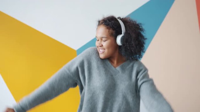 无忧无虑的非洲裔美国女士戴着耳机在室内跳舞的慢动作