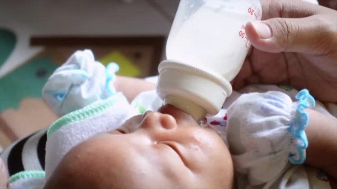 年轻的亚洲母亲在家中卧室用奶瓶喂养男婴