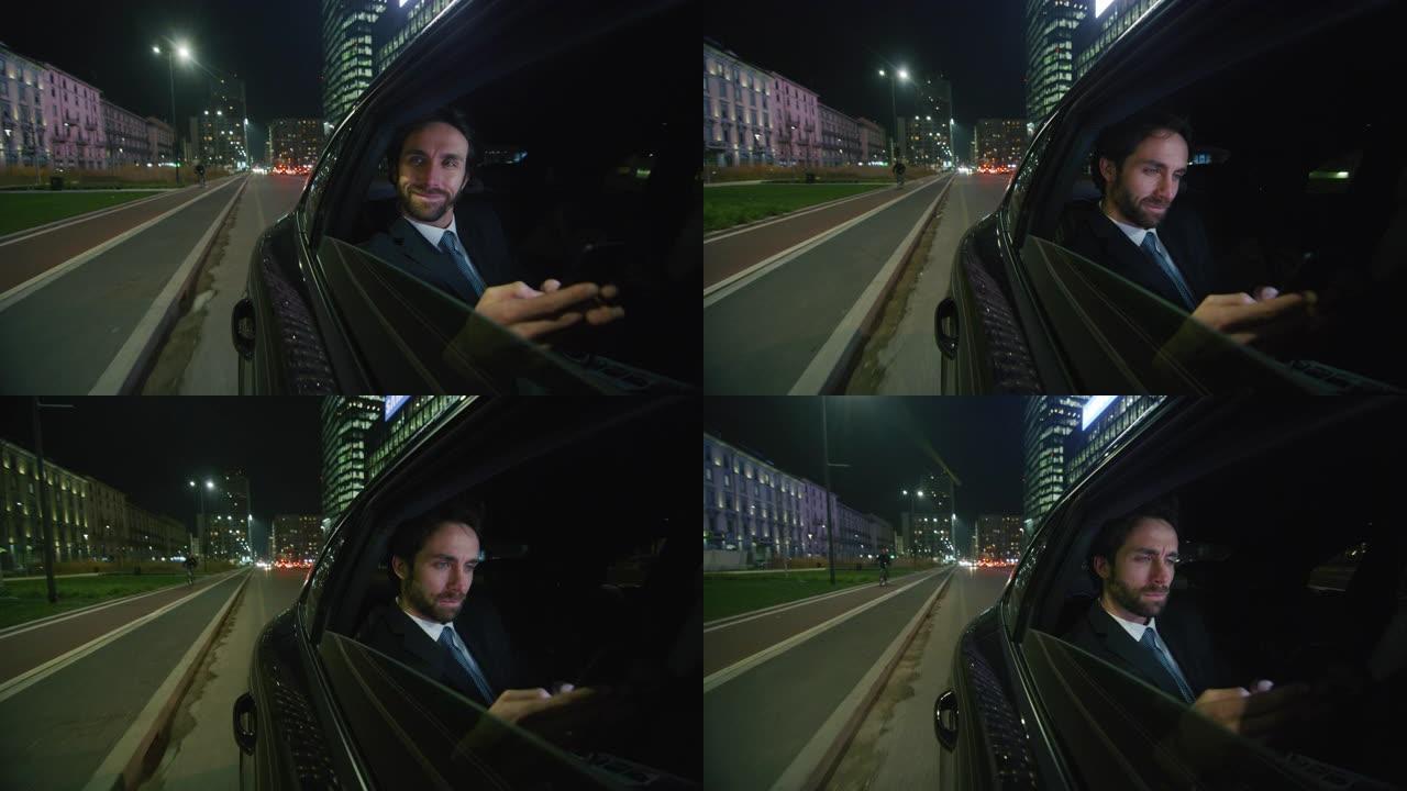英俊的商人使用他的笔记本电脑在一辆现代汽车旅行期间，一个司机在市中心的夜晚。
