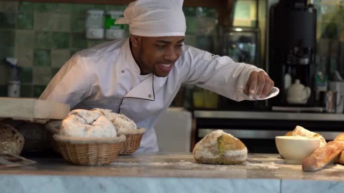 开朗的年轻面包师在面包店微笑着在面包上撒糖粉