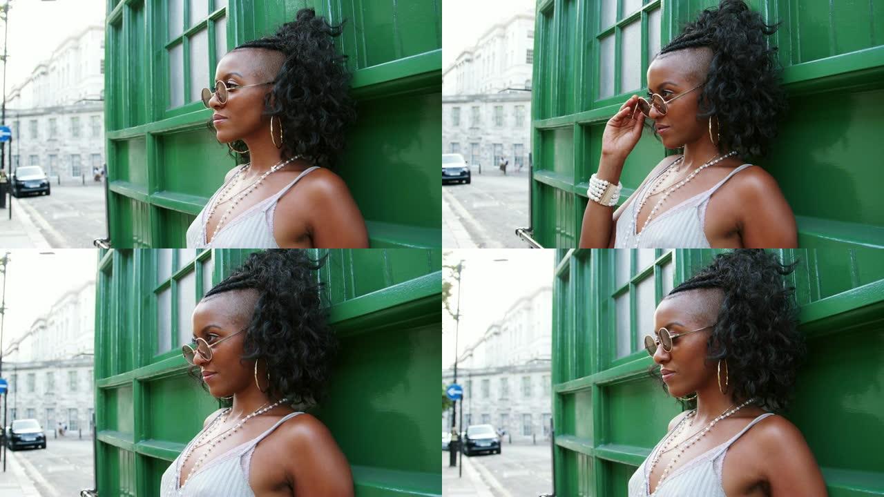 穿着吊带背心的时尚年轻黑人女性靠在街上的绿色墙上，侧视，特写