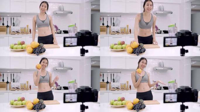 博主运动的亚洲女性使用相机录制如何为订户制作橙汁视频，女性在家中自己使用有机水果制作橙汁。健康食品概