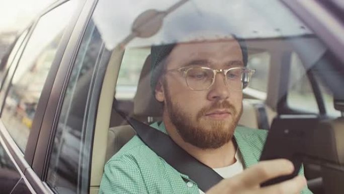 时尚的年轻人坐在汽车上，坐在乘客座位上，使用智能手机，输入消息，通过互联网浏览，喝咖啡。从车外拍摄的