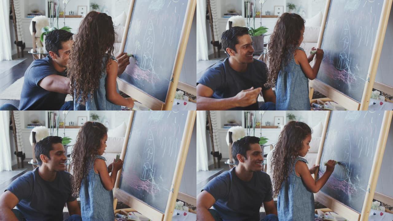 父亲坐在家里的地板上，和他的小女儿在黑板上画画，特写
