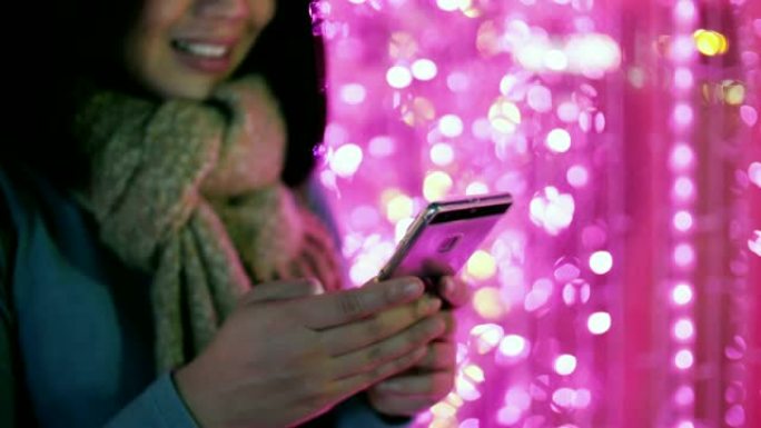 女人在冬天使用手机圣诞节和新年灯光背景，慢动作