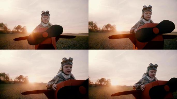快乐的小男孩穿着有趣的纸板飞机服装沿着日落秋天的田野奔跑，玩航空飞行员慢动作。