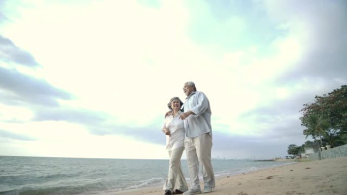 亚洲高级夫妇在美丽的热带海滩上慢动作散步和交谈。