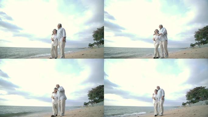 亚洲高级夫妇在美丽的热带海滩上慢动作散步和交谈。