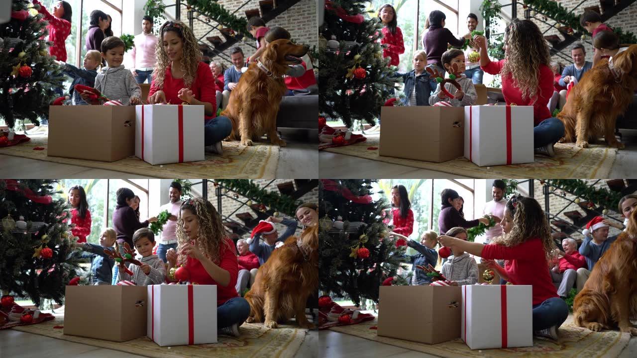 美丽的年轻母亲和儿子从盒子里拿出圣诞装饰品，而家人正在聊天，并在背景中进行有趣的装饰