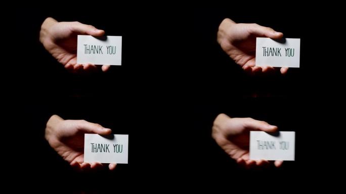 一只手显示一张卡片，上面写着: “谢谢”，孤立在黑色背景上。