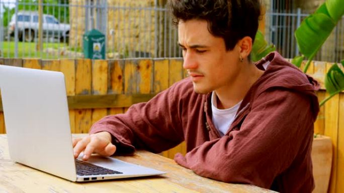 户外咖啡馆4k酷年轻高加索男性滑板手在笔记本电脑上工作的侧视图
