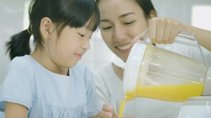 孕妇和她的女儿将水果冰沙倒入搅拌机的玻璃杯中。