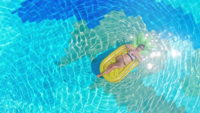 穿着比基尼的女人在游泳池的充气床垫上放松。