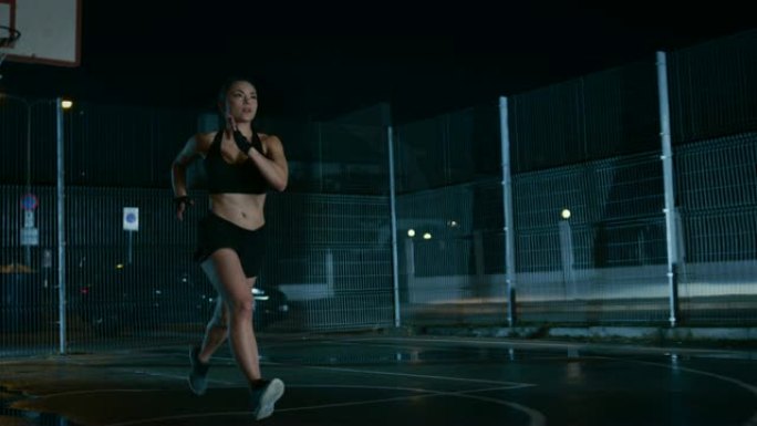 美丽的精力充沛的健身女孩正在一个有围栏的室外篮球场里冲刺。她晚上下雨后在居民区跑步。