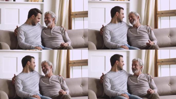 快乐的成年儿子在沙发上笑着和年长的父亲说话