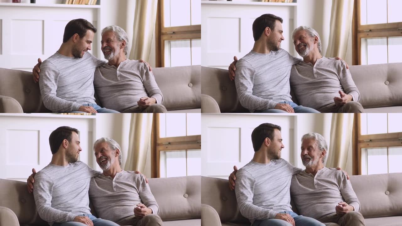 快乐的成年儿子在沙发上笑着和年长的父亲说话