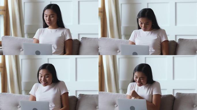 兴奋的幸运亚洲女人用笔记本电脑坐在沙发上
